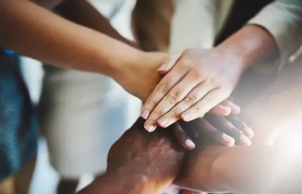 Diverse team members stacking hands together to symbolize teamwork, collaboration, unity, and business partnership.
